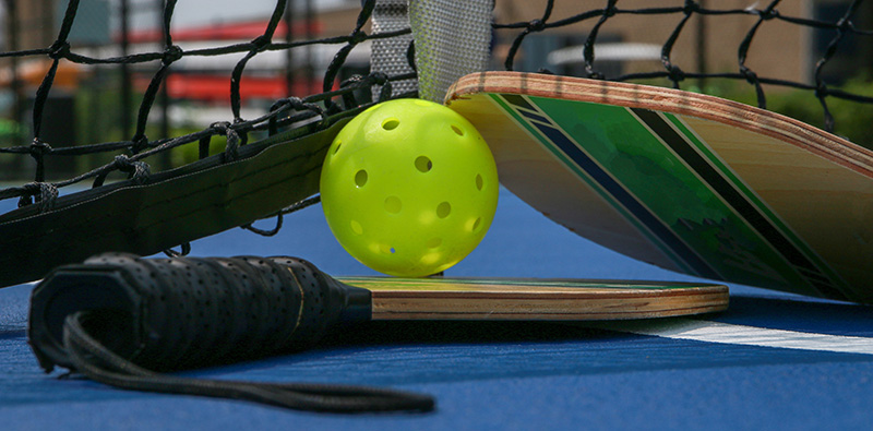 Close up of pickleball paddles and whiffle balls under a net.